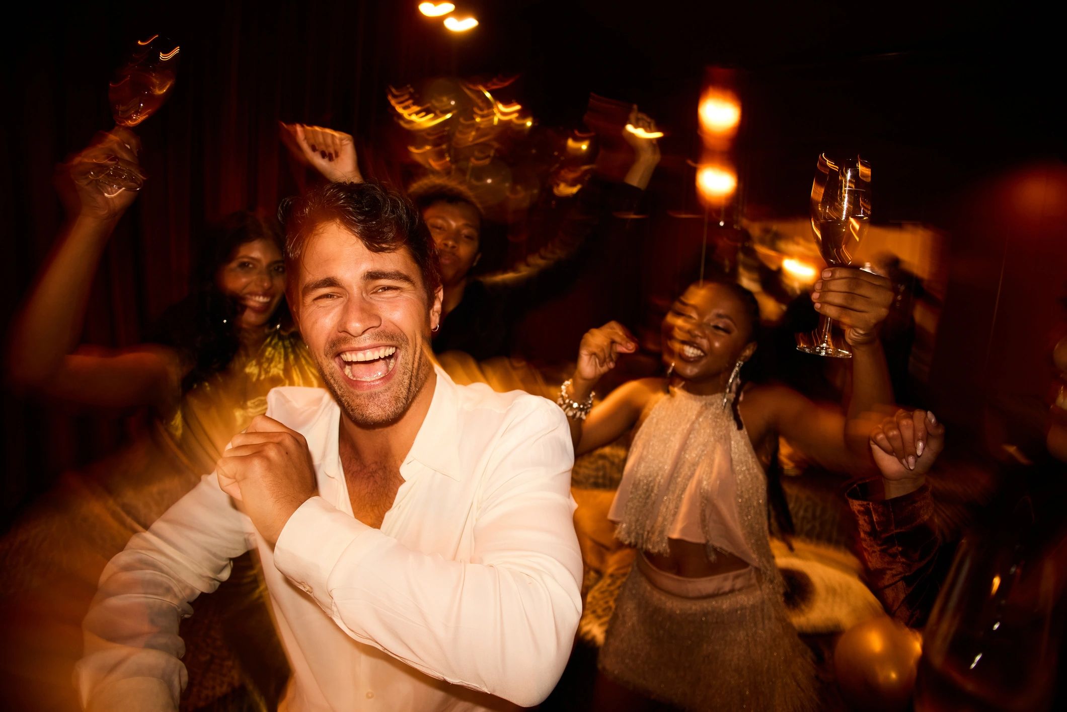 Joyful young man dancing with friends at a lively New Year’s Eve club celebration with illuminated lights